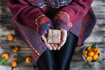 Woman in a huge winter sweater sits on the wooden rustic floor with christmas gifts and mandarins