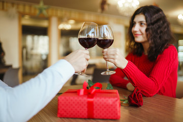 Young couple having a romantic dinner and toasting with glass of red wine. Sweet couple celebrate their anniversary. Valentines day celebration concept. Relationship, surprise and love concept.