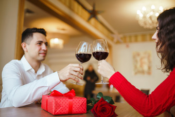 Young couple having a romantic dinner and toasting with glass of red wine. Sweet couple celebrate their anniversary. Valentines day celebration concept. Relationship, surprise and love concept.