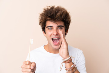 Young handsome man brushing his teeth shouting with mouth wide open