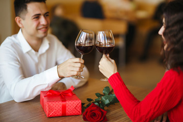 Young couple having a romantic dinner and toasting with glass of red wine. Sweet couple celebrate their anniversary. Valentines day celebration concept. Relationship, surprise and love concept.