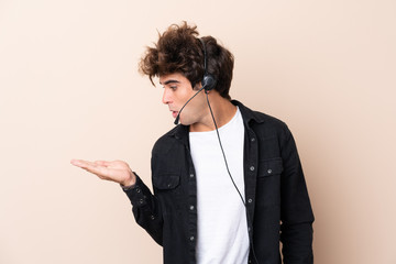 Telemarketer man working with a headset over isolated background holding copyspace imaginary on the palm