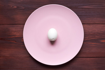Whole boiled chicken egg on a plate on a wooden background.
