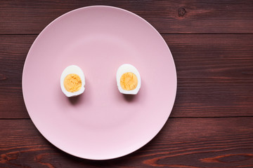 Boiled chicken egg cut into two halves on a pink plate.