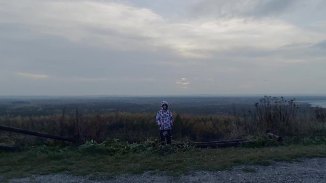 Lonely child with grey autumn forest panorama and misty horizon. Cinematic, dolly shot.