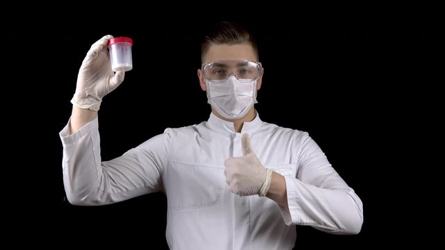 Young man doctor checks sperm tests. A man examines a test jar, then shows a thumb up. Positive semen analysis. On a black background.