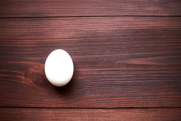 One white egg on a dark wooden background.