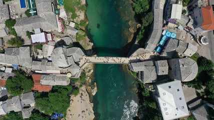 Aerial top down view of old medieval bridge in Mostar, Stari Most, Neretva river, Bosnia and Herzegovina. Sunny summer day. Tourists walking on the bridge.