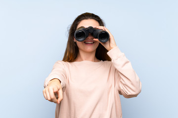 Young brunette girl over isolated blue background with black binoculars