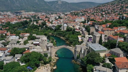 Fototapeta na wymiar Aerial view of Stari Most old medieval bridge in Mostar, Neretva river, Bosnia and Herzegovina. Tourists walking on the bridge. Summer landscape of old town. Mosque on background.
