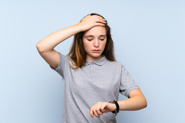 Young brunette girl over isolated blue background with wrist watch and surprised