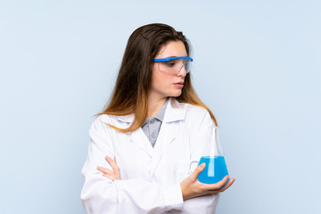 Young brunette girl over isolated blue background with a scientific test tube and looking lateral