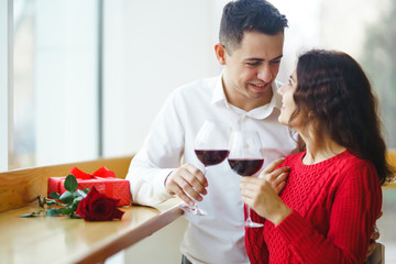 Young couple having a romantic dinner and toasting with glass of red wine. Sweet couple celebrate their anniversary. Valentine's Day, holiday concept. Relationship, surprise and love concept.