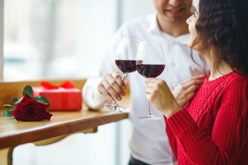 Young couple having a romantic dinner and toasting with glass of red wine. Sweet couple celebrate their anniversary. Valentine's Day, holiday concept. Relationship, surprise and love concept.