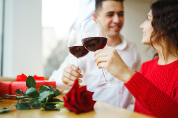Young couple having a romantic dinner and toasting with glass of red wine. Sweet couple celebrate their anniversary. Valentine's Day, holiday concept. Relationship, surprise and love concept.