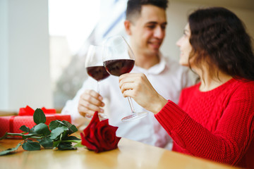 Young couple having a romantic dinner and toasting with glass of red wine. Sweet couple celebrate their anniversary. Valentine's Day, holiday concept. Relationship, surprise and love concept.