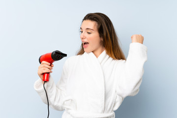 Young woman in a bathrobe with hair hairdryer celebrating a victory
