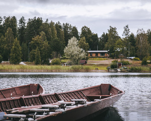 Empty wooden canoe boats on lake shore near building and pine forest in autumn.