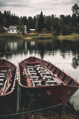 Empty wooden canoe boats on lake shore near building and pine forest in autumn.