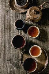 Hot black tea in different traditional wabi sabi style fireclay ceramic craft cups served with plate, teapot and bowl of dry tea leaves on old wooden table. Dark rustic atmosphere. Flat lay, space