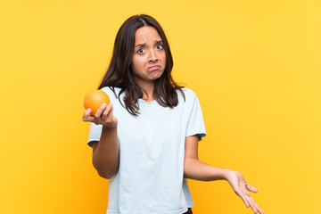 Fototapeta na wymiar Young brunette woman holding an orange making doubts gesture while lifting the shoulders