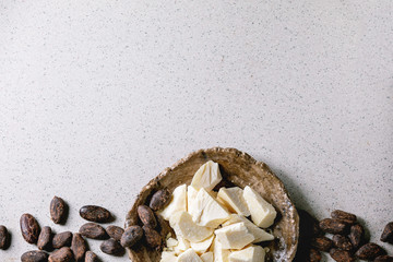 Chopped pieces of raw organic cocoa butter in craft ceramic plate and cocoa beans over grey spotted...