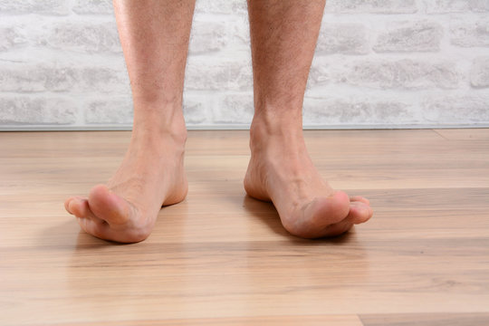 Low Angle POV Of Man's Bare Feet Standing At Home With Raised Toes Upwards