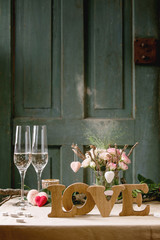 st. Valentines day or wedding romantic table setting with wooden letters love, needle felted hearts, bouquet of pink roses, couple glasses of champagne on natural linen tablecloth.