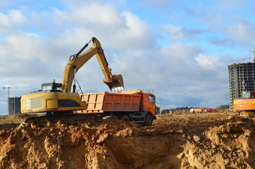 Fototapeta na wymiar Excavator load the sand to the heavy dump truck on construction site. Excavators and dozers digs the ground for the foundation and construction of a new building. Apartment renovation program