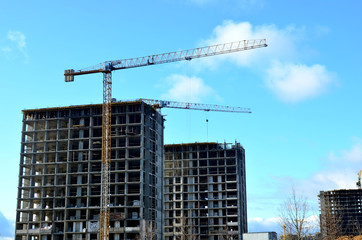 Fototapeta na wymiar Tower cranes constructing a new residential building at a construction site against blue sky. Renovation program, development, concept of the buildings industry.