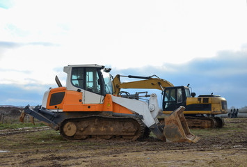 Obraz na płótnie Canvas Crawler Loader and excavator at construction site. Land clearing, grading, pool excavation, utility trenching and foundation digging. Crawler tractor, dozer, earth-moving equipment.