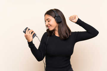 Young brunette girl listening music with a mobile over isolated wall