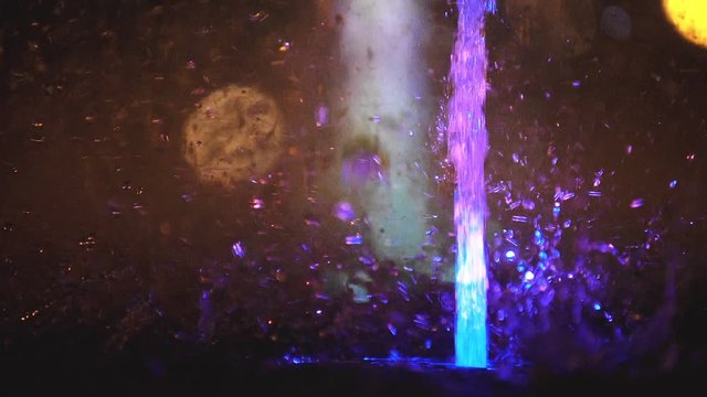 Splashes of fountain. Slow motion of water illuminated in colorful falling on fountain which change it water color in night. Wonderful multicolored fountain throws up high streams of sparkling water.