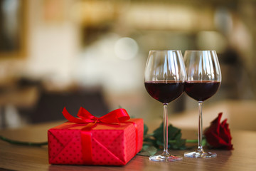 Valentine's day celebration concept. Two glasses of wine, red rose red gift box on wooden table. Romance at restaurant. Valentine's Day, holiday concept. Relationship, surprise and love concept.