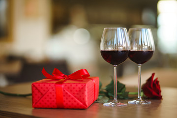 Valentine's day celebration concept. Two glasses of wine, red rose red gift box on wooden table. Romance at restaurant. Valentine's Day, holiday concept. Relationship, surprise and love concept.