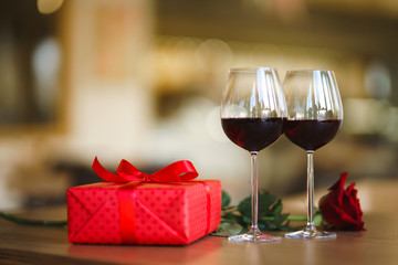 Valentine's day celebration concept. Two glasses of wine, red rose red gift box on wooden table. Romance at restaurant. Valentine's Day, holiday concept. Relationship, surprise and love concept.