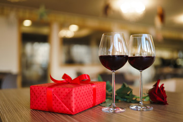 Valentine's day celebration concept. Two glasses of wine, red rose red gift box on wooden table. Romance at restaurant. Valentine's Day, holiday concept. Relationship, surprise and love concept.