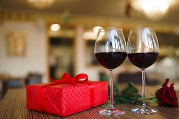 Valentine's day celebration concept. Two glasses of wine, red rose red gift box on wooden table. Romance at restaurant. Valentine's Day, holiday concept. Relationship, surprise and love concept.