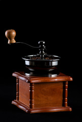 Old vintage coffee grinder with coffee beans on a glass black table with a black background