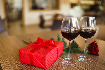 Valentine's day celebration concept. Two glasses of wine, red rose red gift box on wooden table. Romance at restaurant. Valentine's Day, holiday concept. Relationship, surprise and love concept.