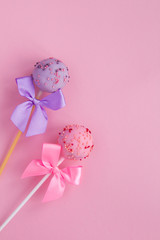 Cake pops with pink and violet bows on the pink background. Top view. Copy space. Location vertical.