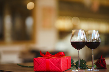 Valentine's day celebration concept. Two glasses of wine, red rose red gift box on wooden table. Romance at restaurant. Valentine's Day, holiday concept. Relationship, surprise and love concept.