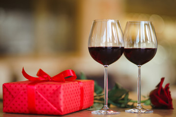 Valentine's day celebration concept. Two glasses of wine, red rose red gift box on wooden table. Romance at restaurant. Valentine's Day, holiday concept. Relationship, surprise and love concept.