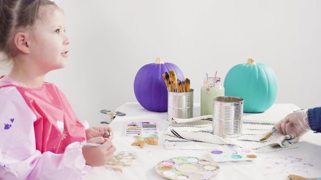 Step by step. Little girl painting mermaid tails and seashells with acrylic paint to decorate Halloween pumpkins.