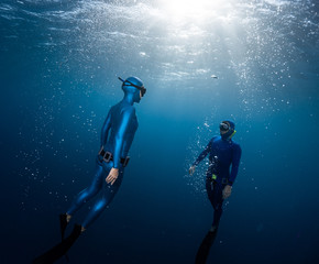 Two freedivers ascend surrounded by bubbles