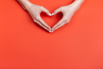 Female hands show a heart symbol on a red background. Place for text.