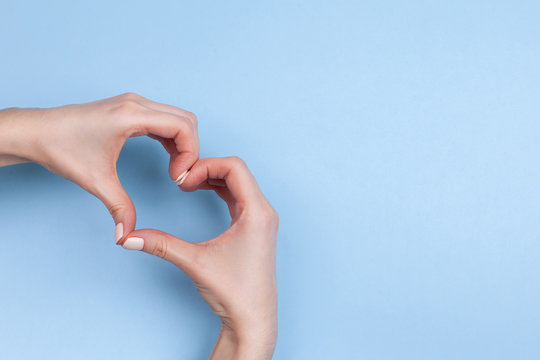 Female hands show a heart symbol on a light blue background. Place for text.