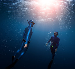 Two freedivers ascend surrounded by bubbles