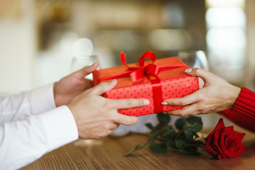 Valentine's Day, holiday and surprise concept. Man gives to his woman a red gift box. Sweet couple celebrate their anniversary. Relationship and love concept.