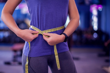 Woman measuring waist with meter in the gym. People, fitness and health concept